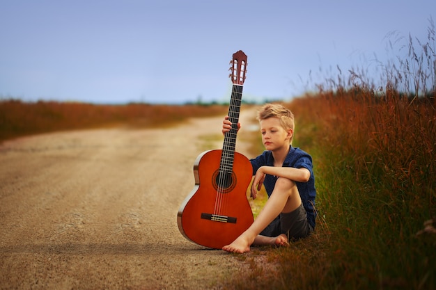 Adolescent avec une guitare acoustique sur une route de campagne.