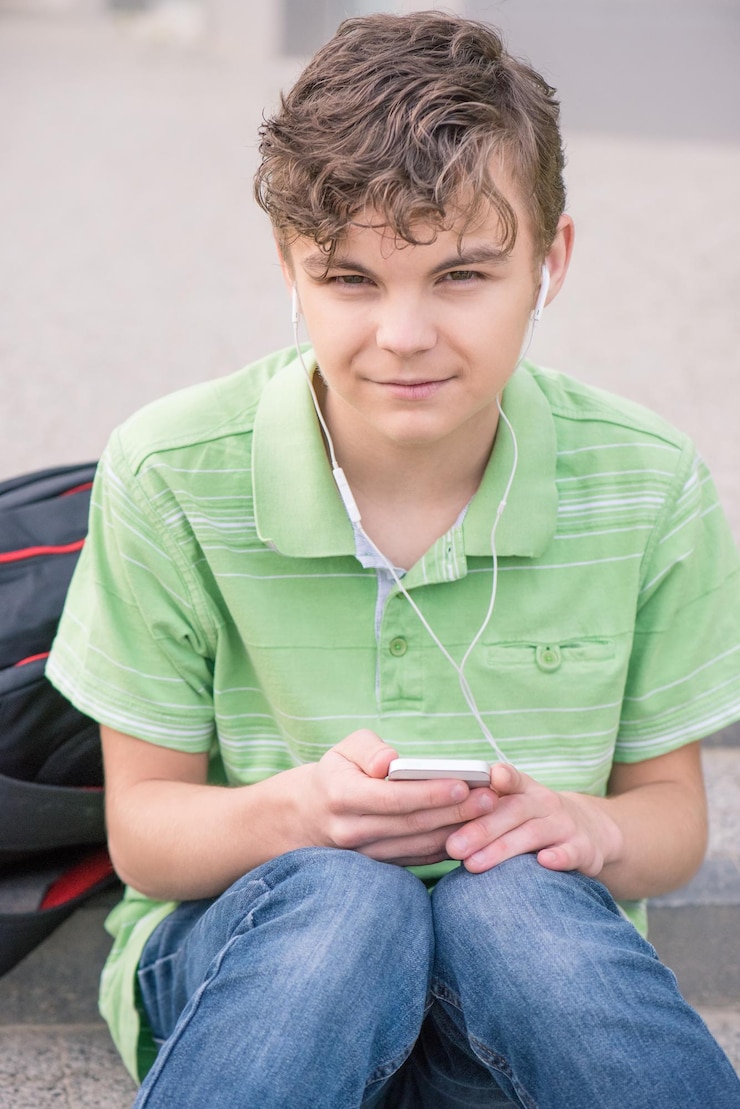 Photo un adolescent heureux avec des écouteurs utilise un gadget en souriant alors qu'il est assis sur les escaliers à l'extérieur un jeune étudiant joue sur son téléphone portable et écoute de la musique