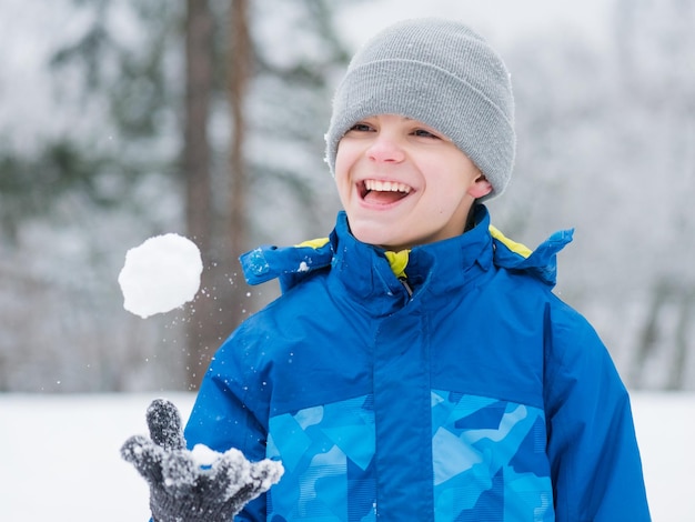 Un adolescent heureux souriant à l'extérieur joue dans la neige par une froide journée d'hiver Un enfant s'amusant dans un parc enneigé Un amusement en plein air pour les vacances de Noël de l'enfance