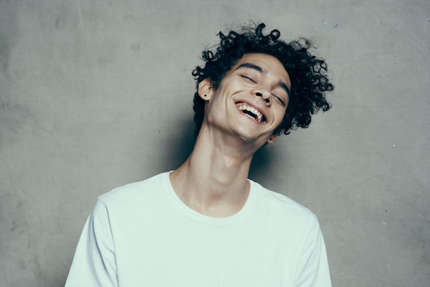 Adolescent heureux en t-shirt blanc cheveux bouclés rire sourire studio de photographie de fond beige