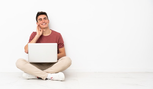 Adolescent homme assis sur le flor avec son ordinateur portable en pensant à une idée