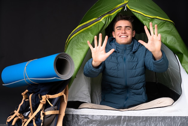 Adolescent homme caucasien à l'intérieur d'une tente de camping vert sur mur noir comptant neuf avec les doigts