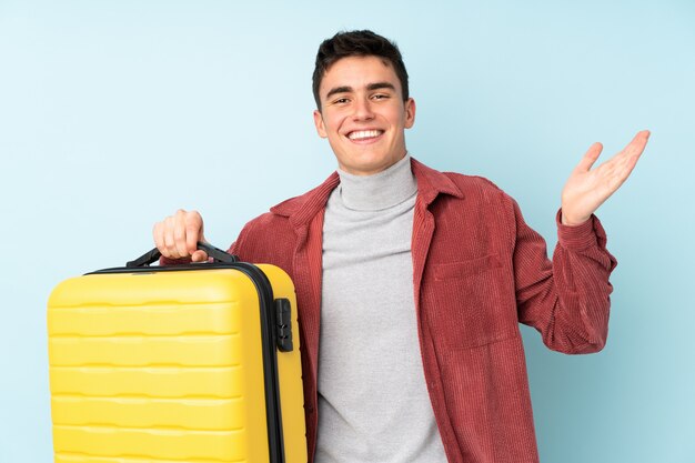 Adolescent homme caucasien sur mur violet en vacances avec valise de voyage et surpris