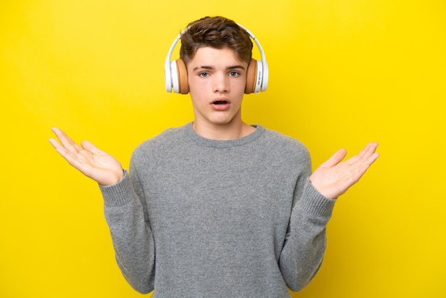 Adolescent homme russe isolé sur fond jaune surpris et écoutant de la musique