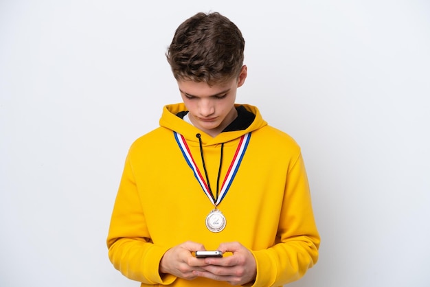 Adolescent homme russe avec des médailles isolé sur fond blanc en envoyant un message avec le mobile
