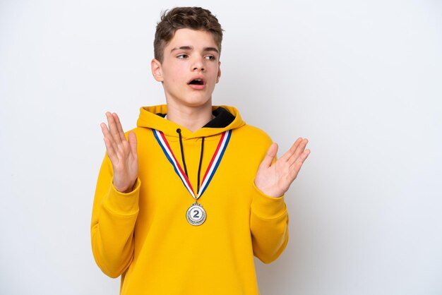 Adolescent homme russe avec des médailles isolé sur fond blanc avec une expression faciale surprise