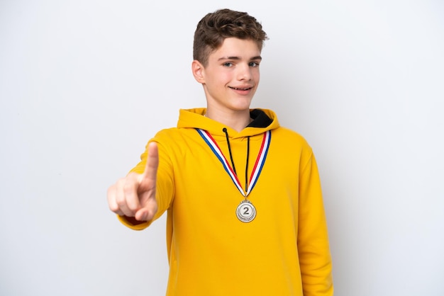 Adolescent homme russe avec des médailles isolé sur fond blanc montrant et levant un doigt