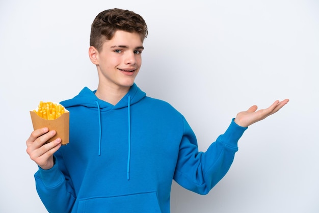 Adolescent homme russe tenant des pommes de terre frites isolé sur fond blanc tendant les mains sur le côté pour inviter à venir