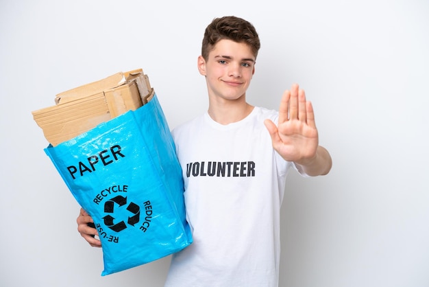 Adolescent homme russe tenant un sac de recyclage plein de papier à recycler isolé sur fond blanc faisant un geste d'arrêt