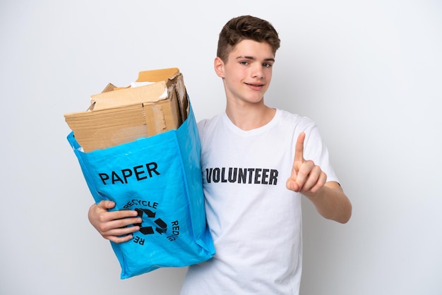 Adolescent homme russe tenant un sac de recyclage plein de papier à recycler isolé sur fond blanc montrant et levant un doigt