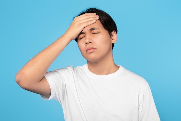 Un adolescent japonais malade ayant de la fièvre et des maux de tête sur fond bleu