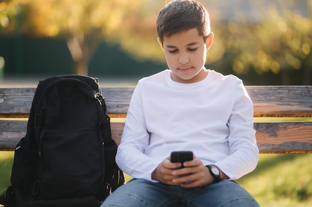 Un adolescent joue à des jeux en ligne sur son smartphone dans le parc après les cours à l'école