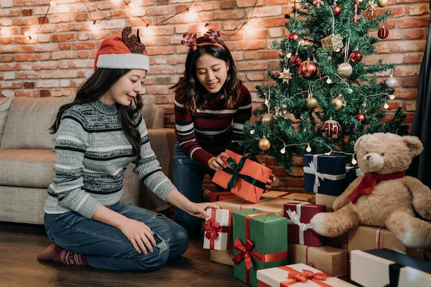 adolescent joyeusement décoré à la maison préparé pour le réveillon de noël. jeunes soeurs mettant des cadeaux sous le sapin de noël. merveilleux travail d'équipe pour la nouvelle année et Noël.