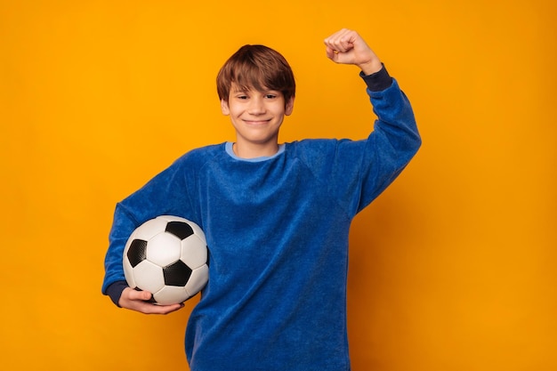 Un adolescent joyeux tenant un ballon de football fait le geste du gagnant