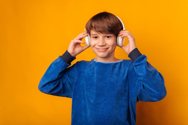 Un adolescent joyeux vêtu de bleu tient et porte des écouteurs blancs