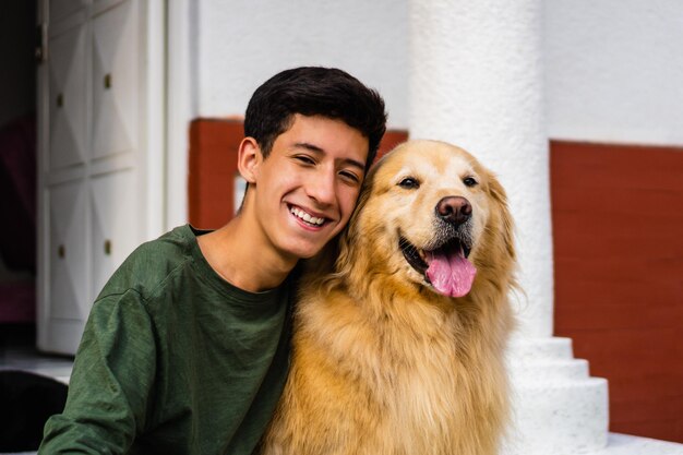 Adolescent latin riant et étreignant son chien golden retriever assis dans l'allée