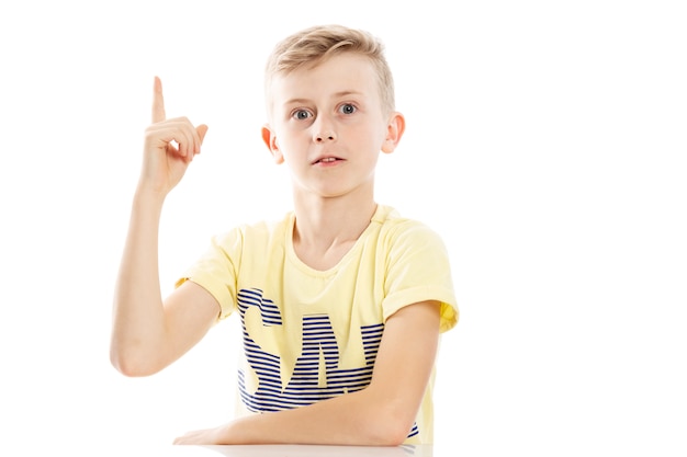 Un adolescent a levé son index, a une idée. Assis près de la table. Isolé sur fond blanc.