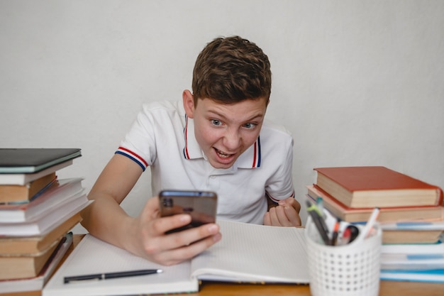 Un adolescent à la maison pour les manuels en regardant un smartphone voit l'heureuse nouvelle