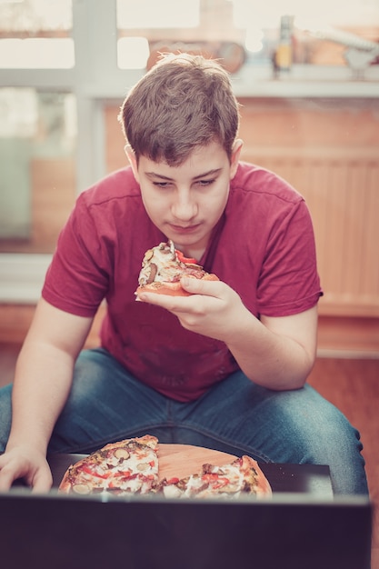 Adolescent, manger de la pizza assis à un ordinateur portable.