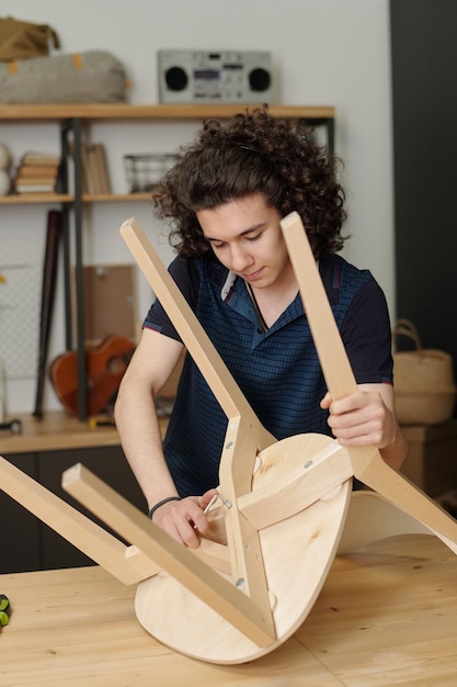 Adolescent masculin se penchant au-dessus de la table dans le garage tout en réparant la chaise en bois