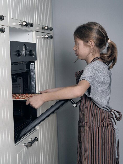 Un adolescent met une pizza dans le four de la cuisine.