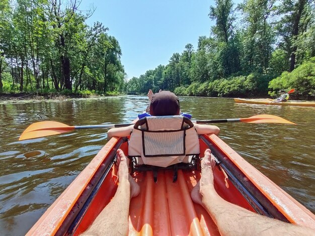 Un adolescent nage avec une rame dans un kayak sur la rivière sur le fond des arbres vue arrière