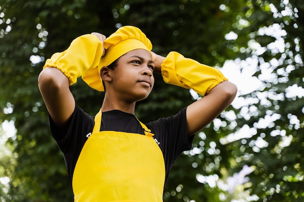 Adolescent noir africain cuisinier en toque de chefs et uniforme de tablier jaune touchant son chapeau de chefs Publicité créative pour café ou restaurant