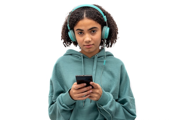 Adolescent noir regardant la caméra tout en utilisant un smartphone et en écoutant de la musique isolé sur fond blanc