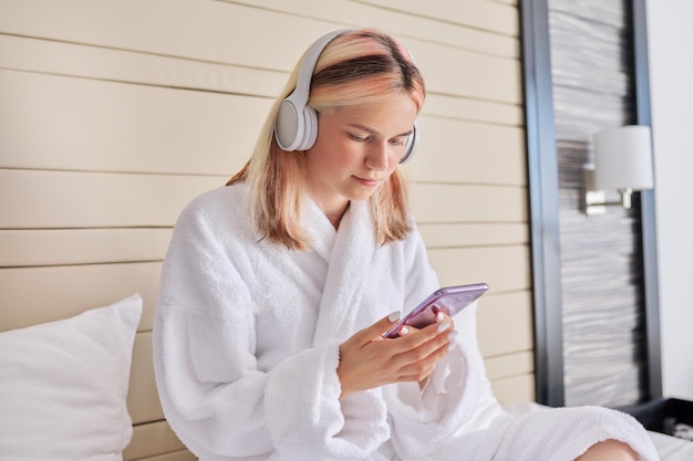 Adolescent en peignoir blanc et écouteurs avec smartphone dans les mains