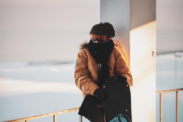 Un adolescent pensif avec un snowboard dans les mains pose pour le photographe le jour de l'hiver.