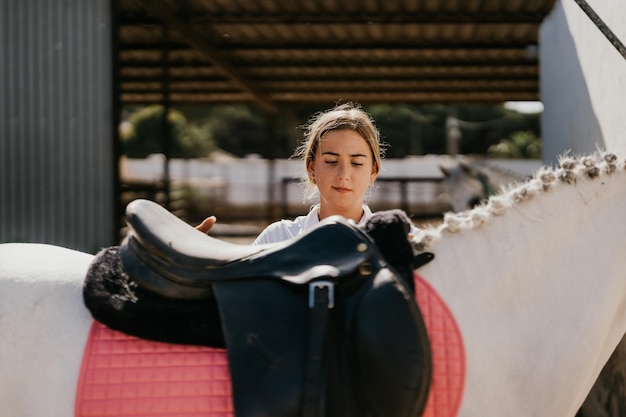 Adolescent plaçant une selle sur un cheval blanc