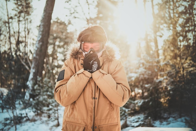 Un adolescent portant des lunettes de protection se réchauffe les mains dans la forêt d'hiver.