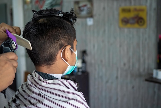 Un adolescent portant un masque de protection du visage se fait couper les cheveux dans un salon de coiffure.