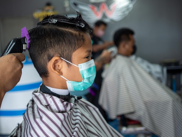 Un adolescent portant un masque de protection du visage se fait couper les cheveux dans un salon de coiffure.