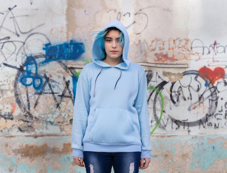 Photo adolescent portant un sweat à capuche surdimensionné bleu clair et un jean regardant dans l'appareil photo une adolescente aux cheveux bleus reste à l'extérieur contre un mur de graffitis maquette de vêtements