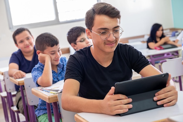 Un adolescent qui utilise la tablette à l'école et qui a un sourire sur le visage.