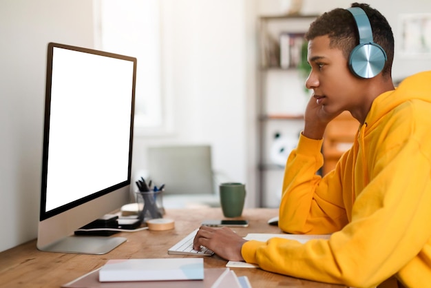 Un adolescent réfléchi à son bureau avec des écouteurs et un ordinateur.