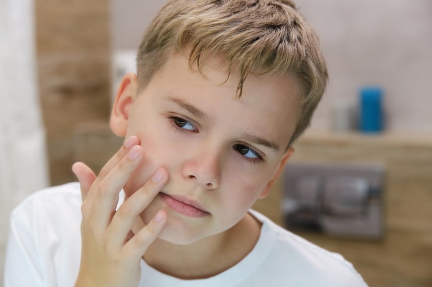 L'adolescent regarde la peau de son visage avec agacement