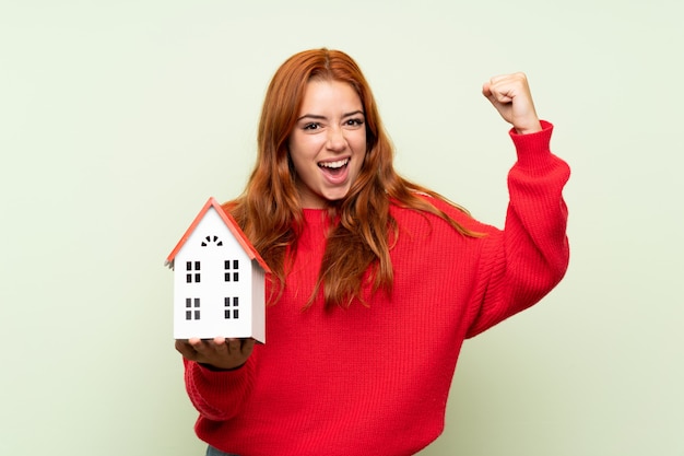 Photo adolescent rousse avec pull sur vert isolé tenant une petite maison