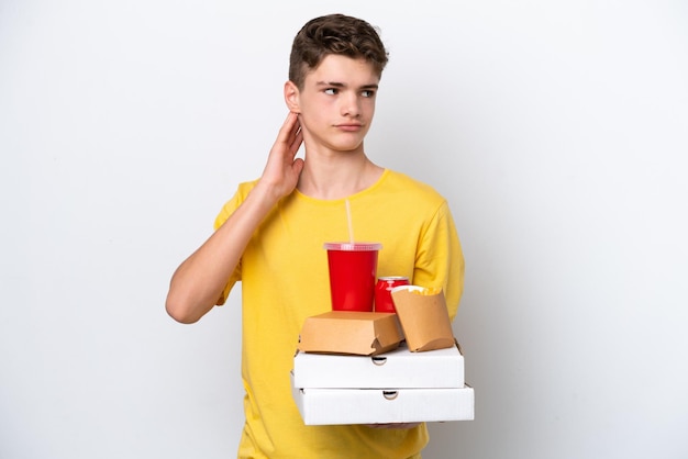 Adolescent russe man holding fast food isolé sur fond blanc ayant des doutes