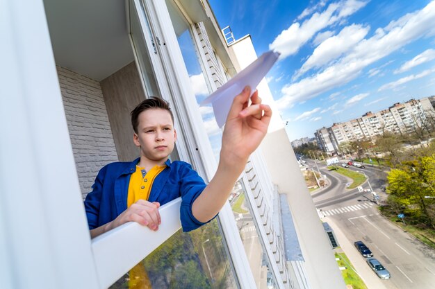 Adolescent s'amusant tout en restant à la maison pendant la quarantaine. Kid lance un avion en papier depuis le balcon.