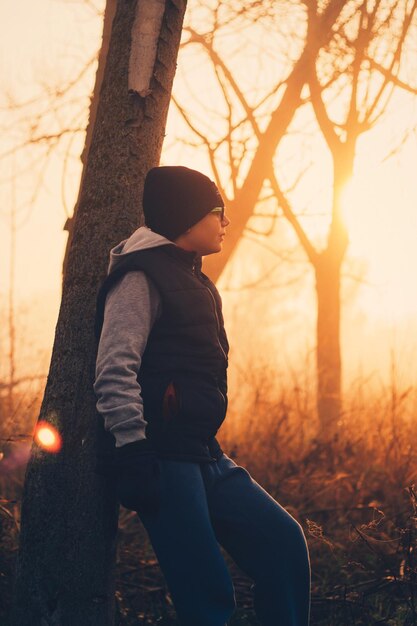 Photo un adolescent s'appuie sur un arbre dans un champ au coucher du soleil.