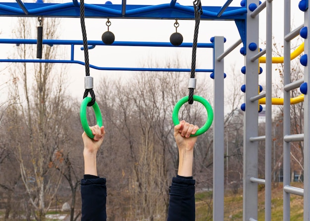 Un adolescent s'entraîne sur un terrain de sport dans la rue sur des anneaux de sport Les mains tiennent sur des anneaux de sport