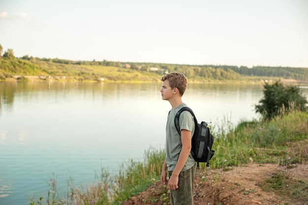 Un adolescent avec un sac à dos se tient sur la rive de la rivière et se penche sur la randonnée à distance et