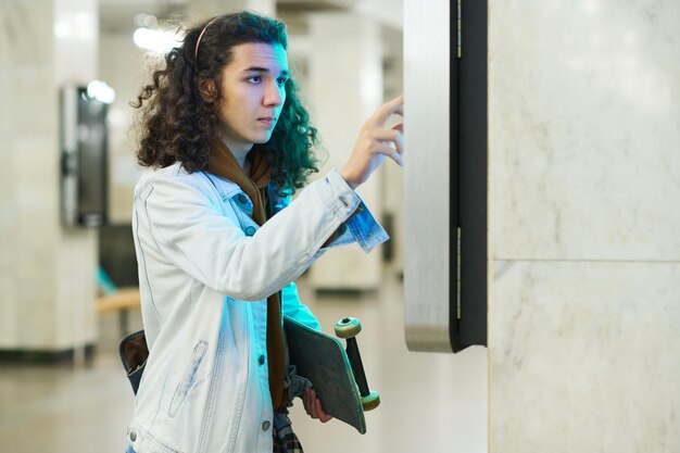 Adolescent sérieux faisant défiler l'horaire des rames de métro tout en se tenant devant l'écran interactif de la station de métro et en le touchant