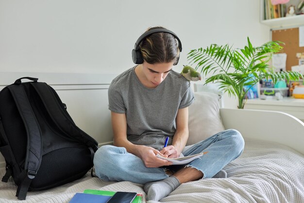 Adolescent de sexe masculin avec un étudiant perroquet de compagnie assis dans un casque à la maison