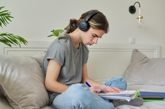 Adolescent de sexe masculin avec un étudiant perroquet de compagnie assis dans un casque à la maison