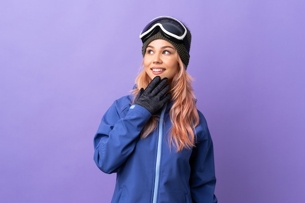 Adolescent skieur fille avec des lunettes de snowboard sur violet isolé regardant en souriant