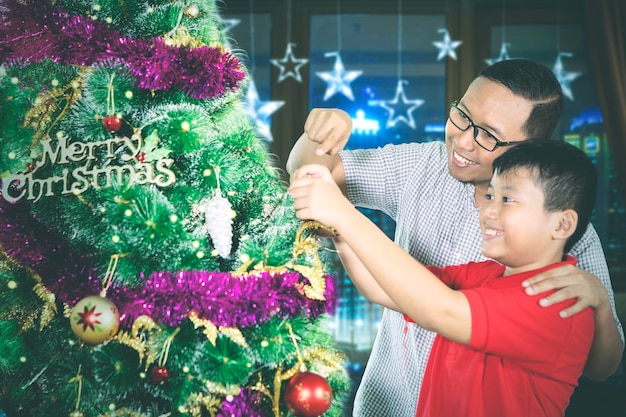 Un adolescent et son père décorent un sapin dans leur appartement.