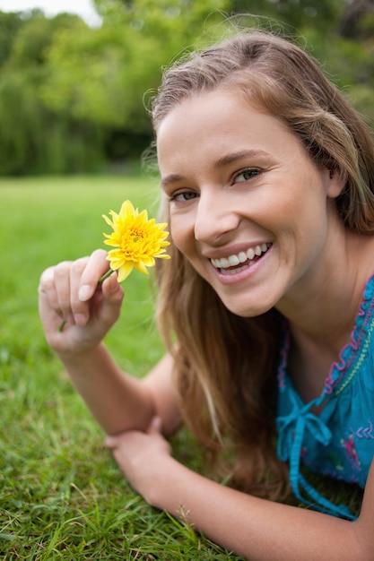 Adolescent souriant tenant une fleur jaune en position couchée sur l&#39;herbe